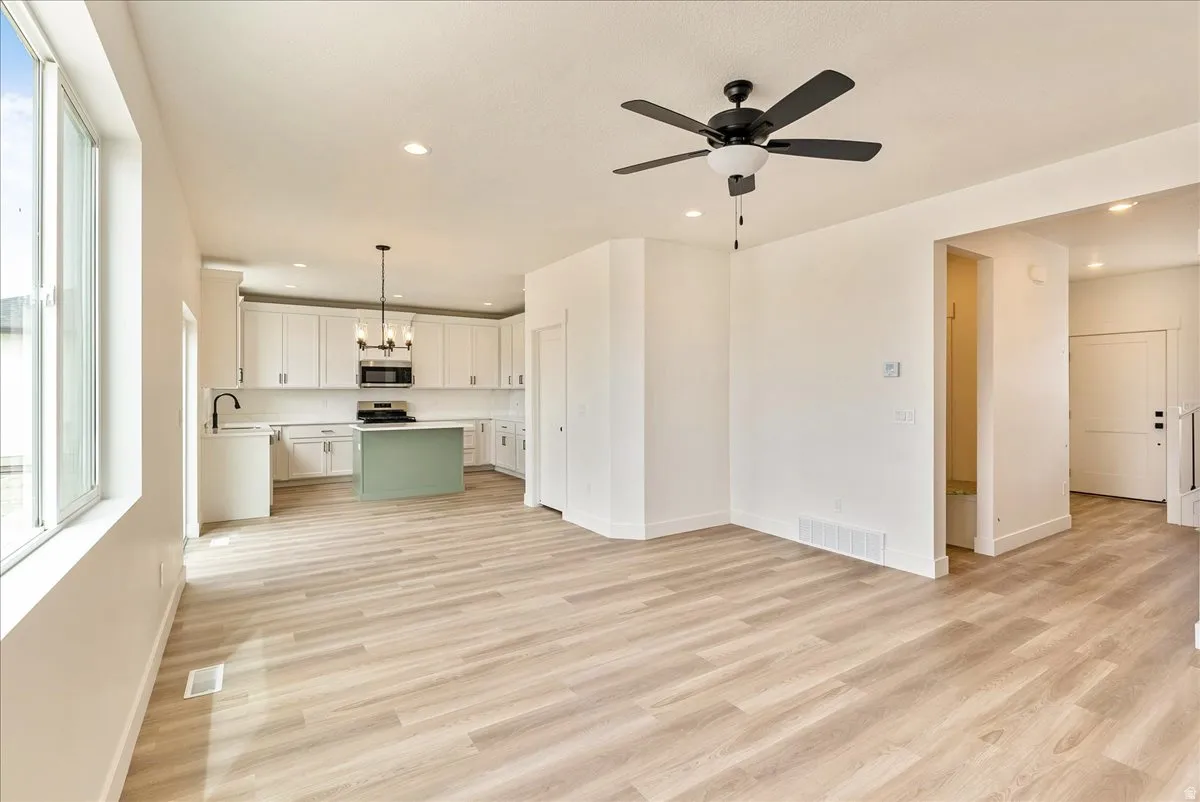 Unfurnished living room featuring a ceiling fan, light wood-style floors, and a chandelier