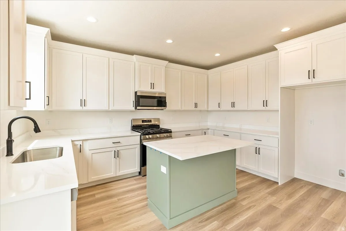 Kitchen featuring stainless steel appliances, light stone counters, light wood-style flooring, recessed lighting, and a center island
