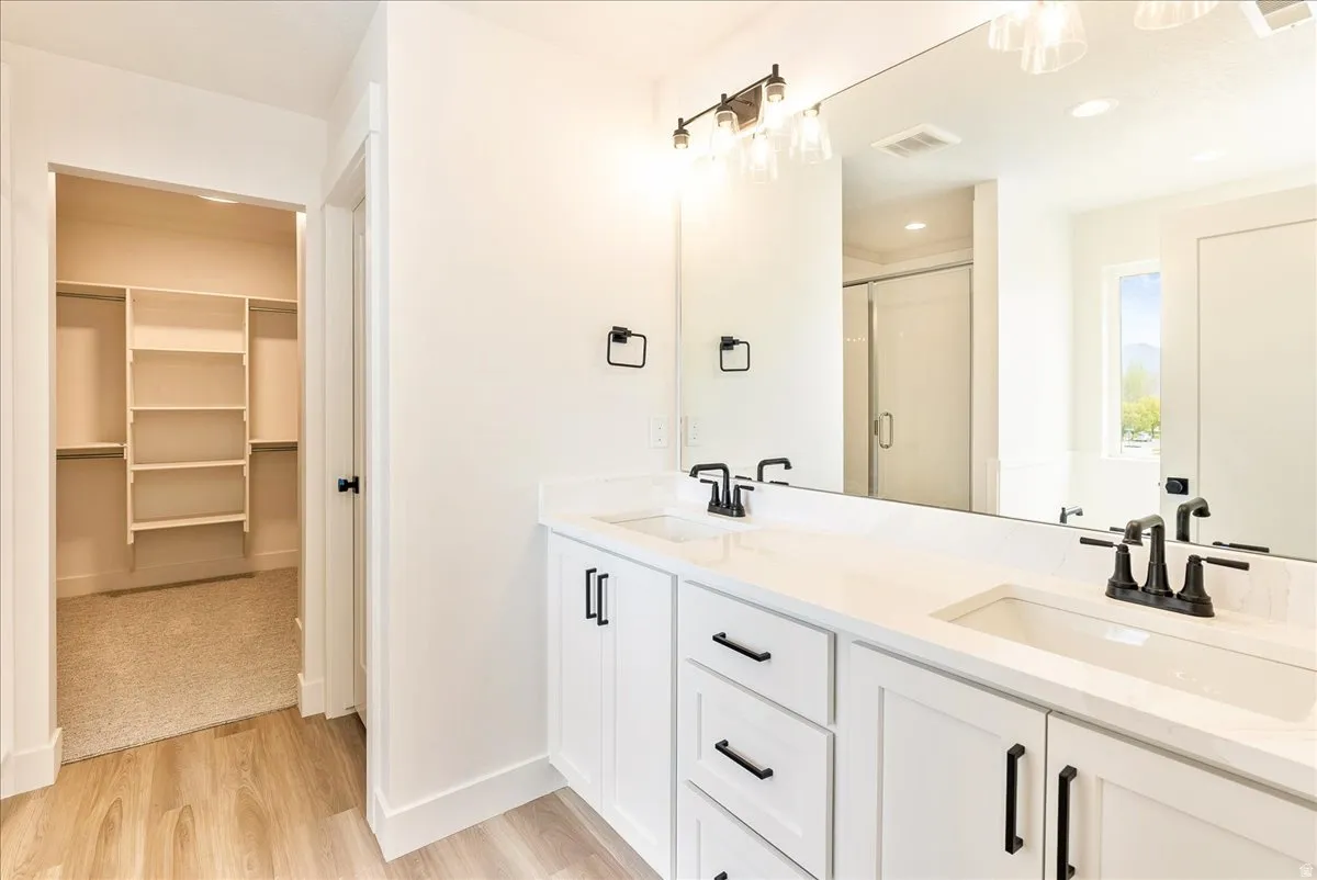 Bathroom featuring a walk in closet, double vanity, light wood-type flooring, and a shower stall