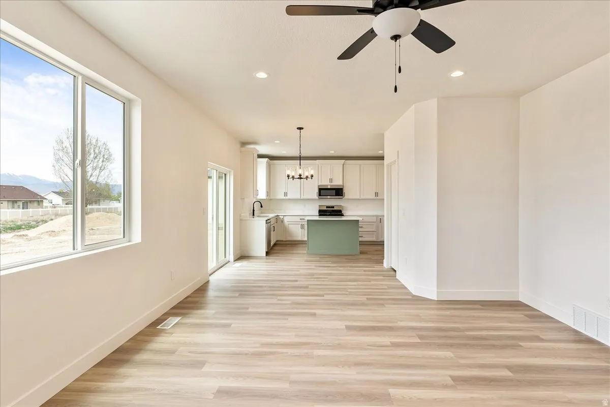 Unfurnished living room with light wood-type flooring, a ceiling fan, and a chandelier