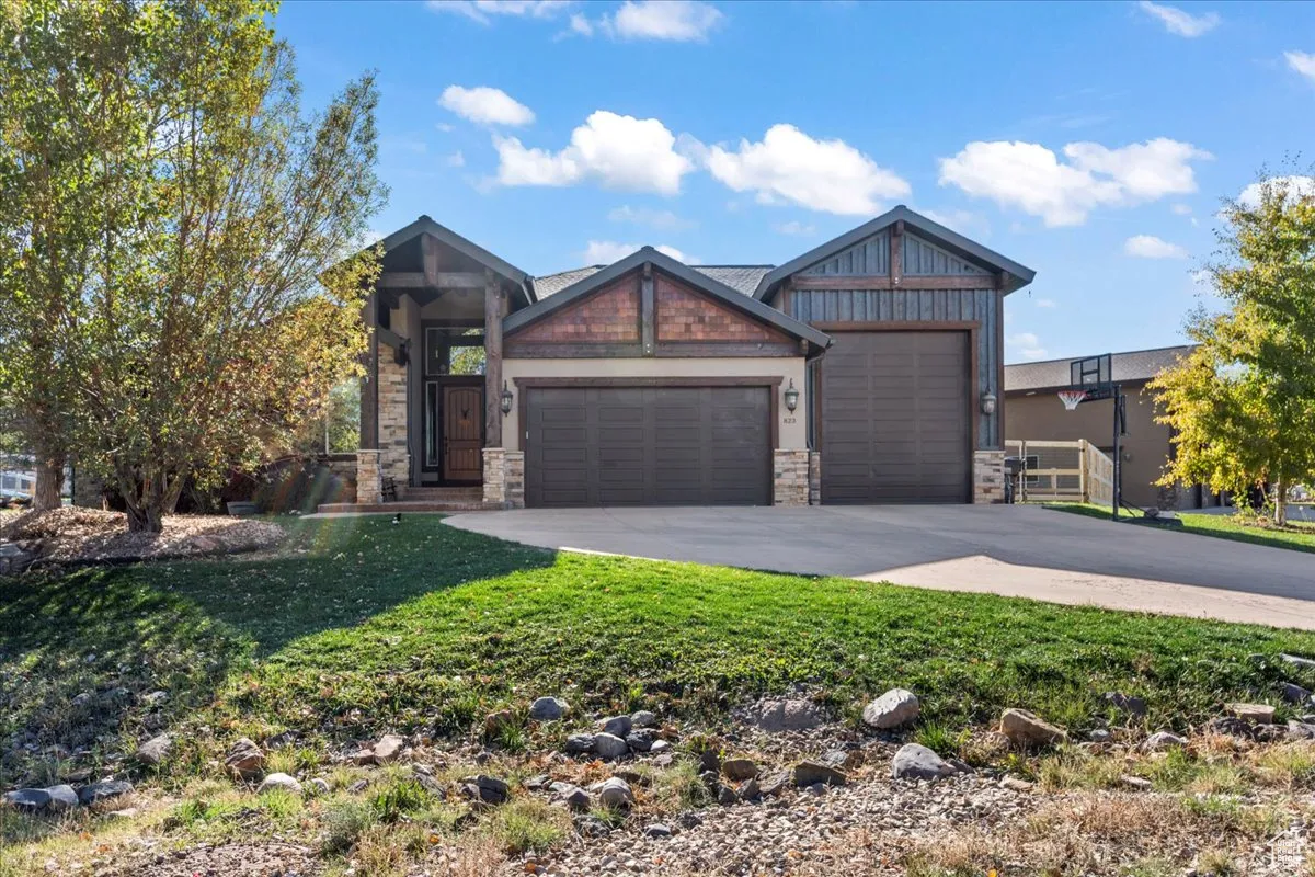 Craftsman house with an attached garage, stone siding, driveway, and a front yard