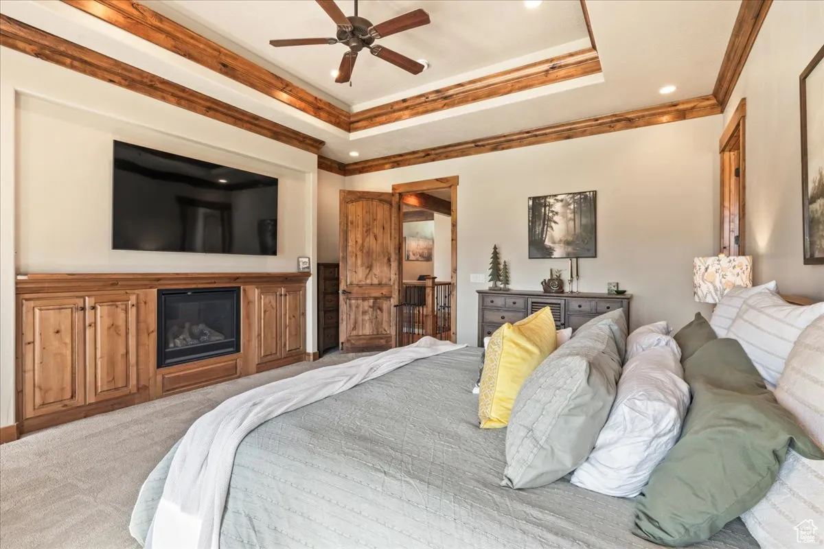 Primary Bedroom with a raised ceiling, crown molding, ceiling fan, and a glass covered fireplace