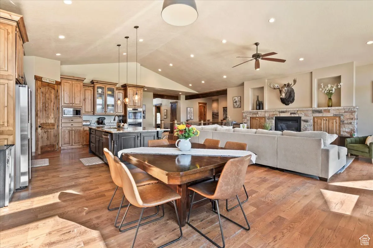 Dining space with vaulted ceiling, light wood-style flooring, ceiling fan, recessed lighting, and a stone fireplace