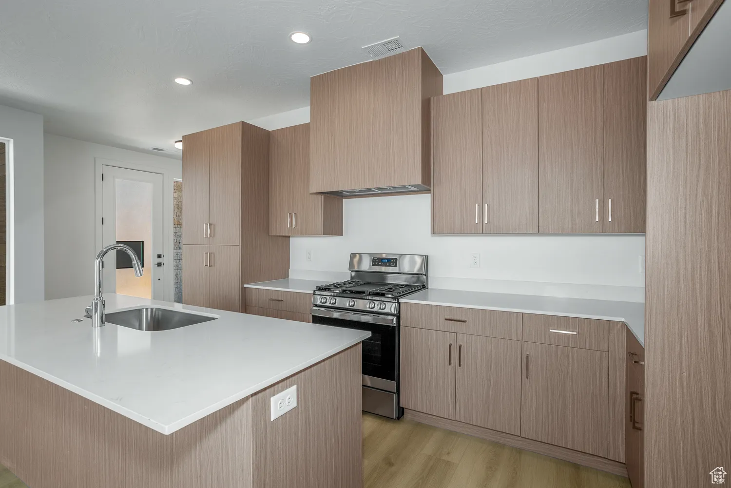 Kitchen with gas stove, a kitchen island with sink, light wood-style flooring, recessed lighting, and light stone countertops