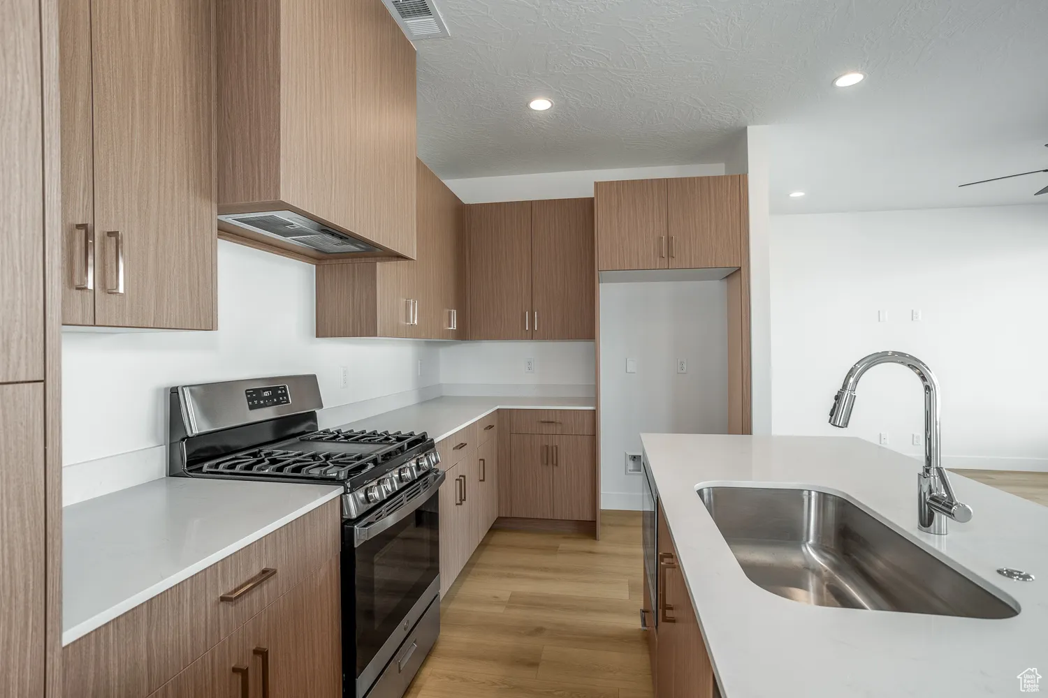 Kitchen featuring stainless steel range with gas cooktop, light wood-style floors, modern cabinets, exhaust hood, and a textured ceiling