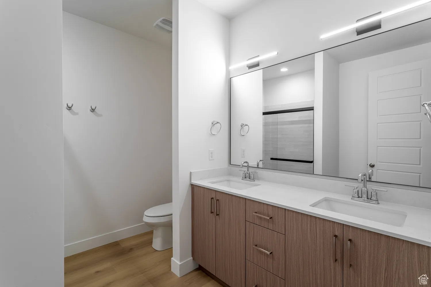 Bathroom featuring double vanity, light wood-style floors, and an enclosed shower