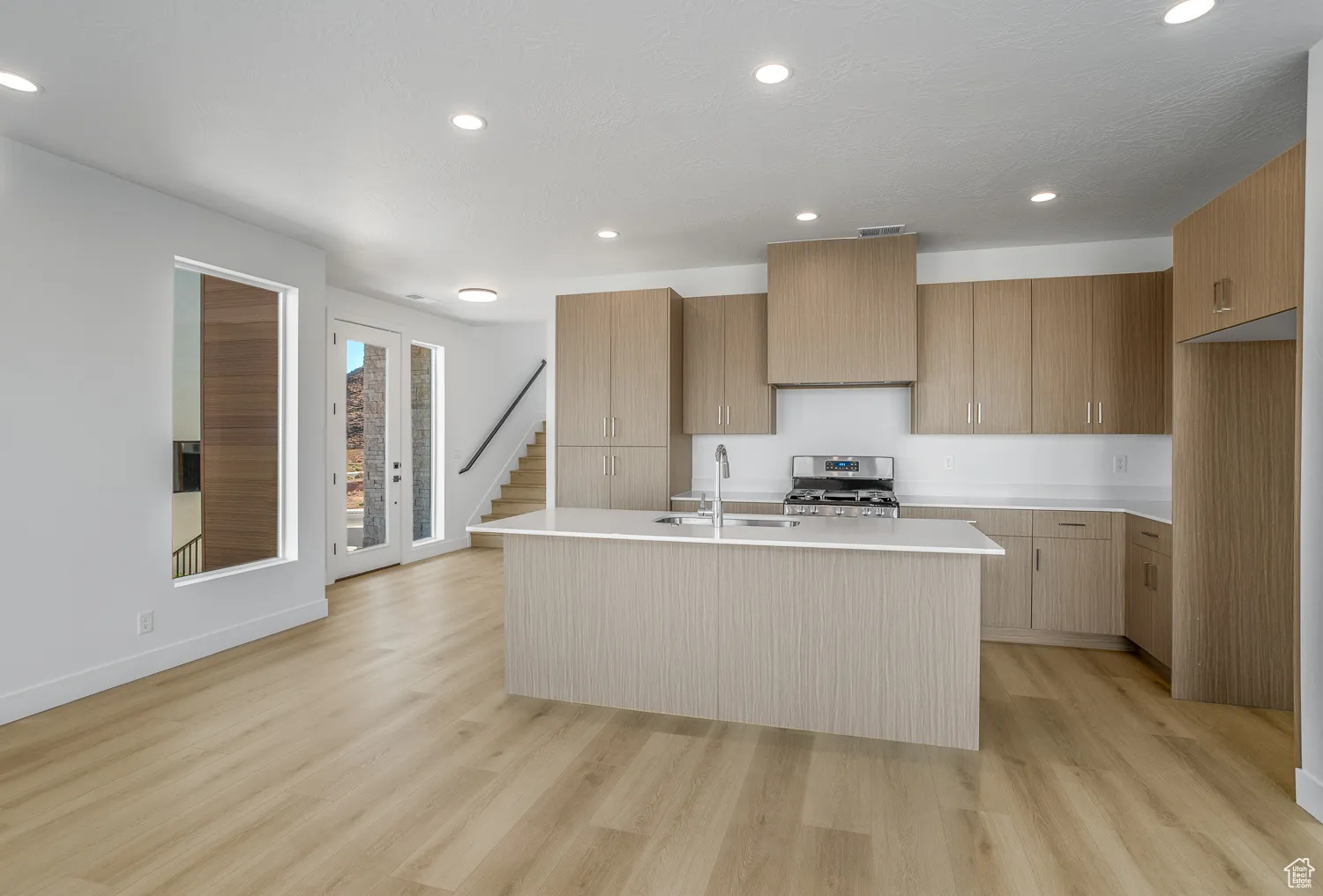 Kitchen featuring modern cabinets, recessed lighting, light wood-type flooring, stainless steel range with gas stovetop, and an island with sink