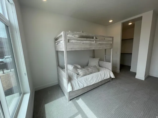 Recessed lighting illuminating a spacious room with light-colored carpeting, featuring a large window, and an open closet with shelving and hanging rods