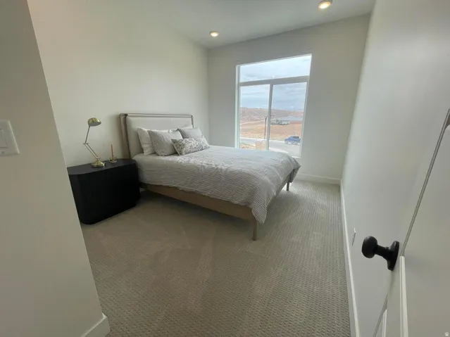 Light-colored carpeting, large window, recessed lighting, and white wall finishes