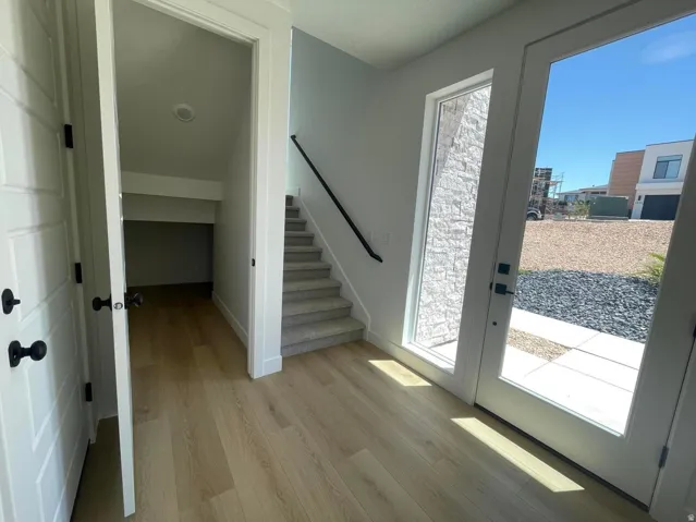 Wood-finish flooring, white panel doors with matte black hardware, carpeted stairs with a black handrail, and a full-light entry door with an adjacent window featuring stone-textured privacy glass