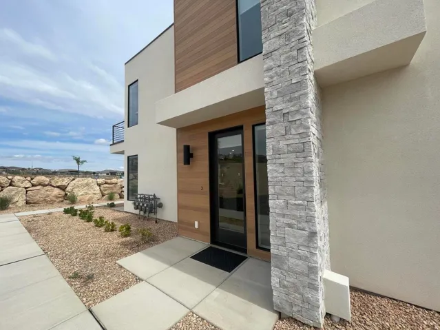 Modern exterior featuring a stucco finish, stone veneer accent, wood-finish siding, full-lite entry door, and a second-story balcony with metal railing