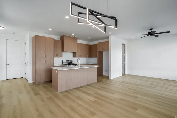 Kitchen and living area featuring wood-finish flooring, a modern linear chandelier, and a ceiling fan