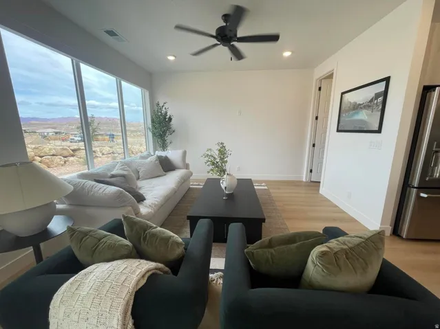 Expansive window wall, light wood-finish flooring, recessed ceiling lighting, ceiling fan, and stainless steel French door refrigerator