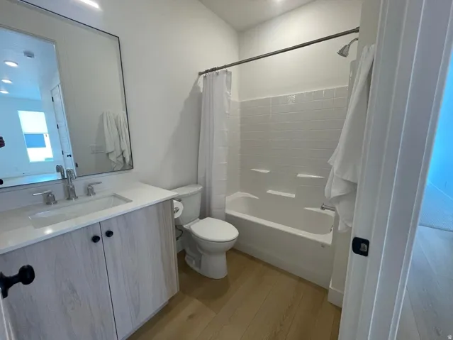 Wood-finish flooring, single vanity with light-toned cabinetry and integrated sink, chrome faucet, and subway tile shower surround with tub