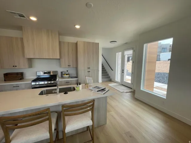 Open-concept kitchen with light wood-finish cabinetry, stainless steel appliances, and a central island with integrated sink