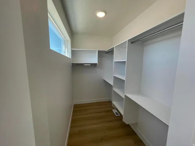 Walk-in closet with built-in shelving, hanging rods, wood-finish flooring, and a transom window