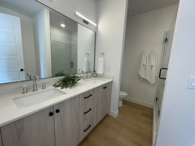 Dual vanity with integrated sinks, chrome fixtures, light wood-finish cabinetry, and a spacious glass-enclosed shower