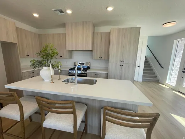 Kitchen featuring light wood-finish cabinetry, stainless steel range, and a large central island with an undermount sink and light-toned countertop