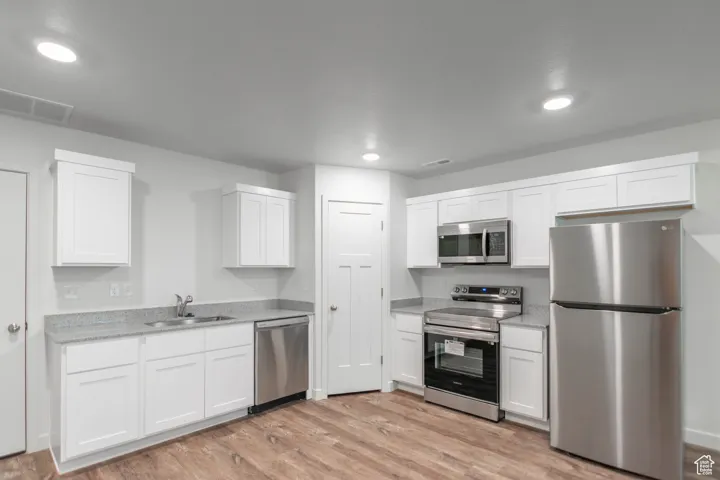 Kitchen featuring appliances with stainless steel finishes, LVT flooring, white cabinetry, recessed lighting, and light stone counters