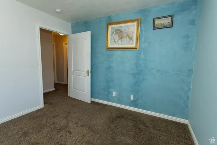 Unfurnished room featuring a textured ceiling and dark colored carpet