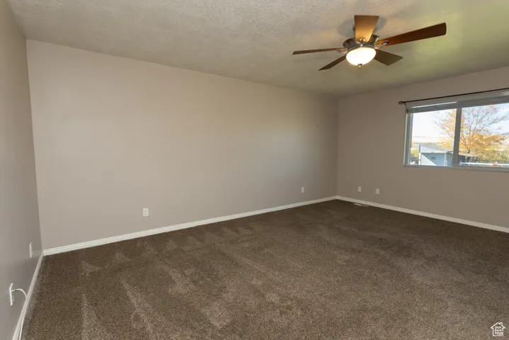 Unfurnished room with dark carpet, a textured ceiling, and ceiling fan