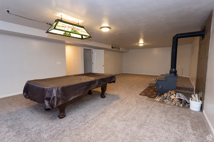 Game room featuring a wood stove, billiards table, carpet floors, and a textured ceiling