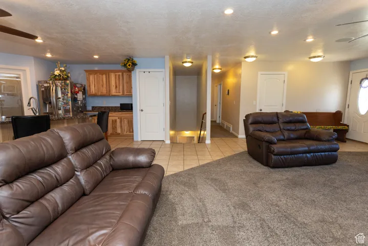 Living area with a ceiling fan, a textured ceiling, light tile patterned floors, light colored carpet, and recessed lighting