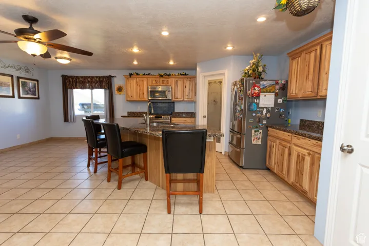 Kitchen with stainless steel appliances, a center island with sink, a breakfast bar area, light tile patterned floors, and a textured ceiling