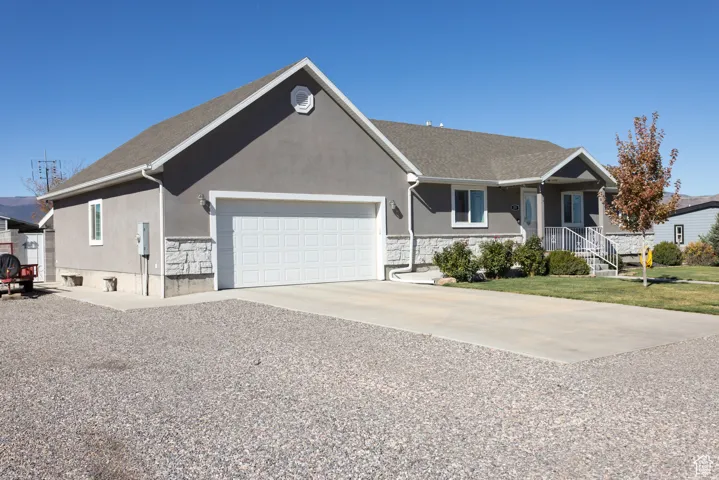 Single story home featuring driveway, stucco siding, covered porch, and an attached garage