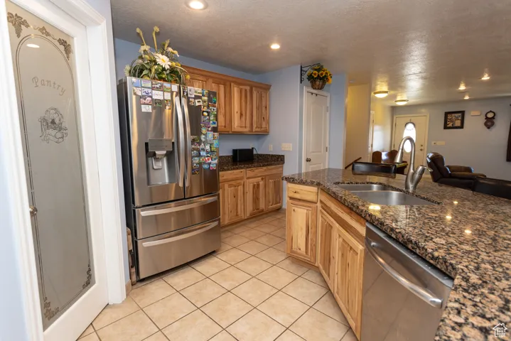 Kitchen with stainless steel appliances, a textured ceiling, dark stone countertops, open floor plan, and light tile patterned floors