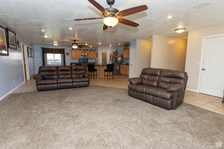 Living area featuring light tile patterned floors, light colored carpet, a textured ceiling, and a ceiling fan