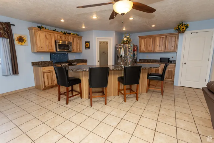 Kitchen with a breakfast bar area, a center island with sink, a textured ceiling, light tile patterned flooring, and ceiling fan