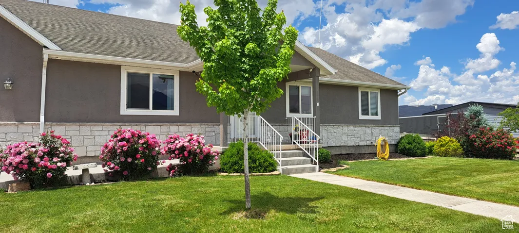 View of front of property featuring stone siding, a front lawn, roof with shingles, and stucco siding