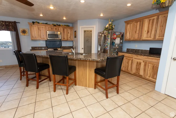 Kitchen featuring stainless steel appliances, a breakfast bar area, light tile patterned flooring, a textured ceiling, and recessed lighting