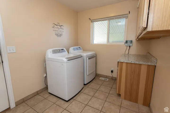 Washroom with cabinet space, light tile patterned floors, and independent washer and dryer