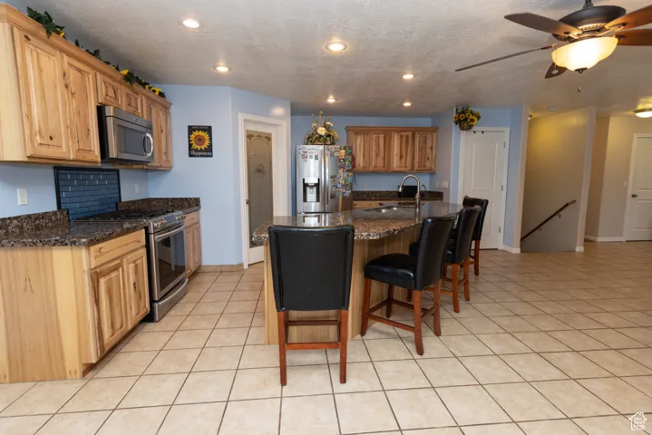 Kitchen featuring a kitchen bar, an island with sink, appliances with stainless steel finishes, a textured ceiling, and light tile patterned flooring