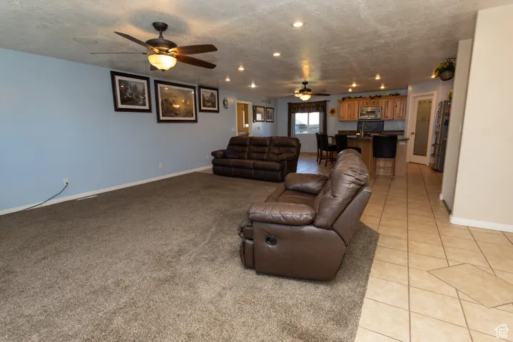 Living room featuring a textured ceiling, light tile patterned floors, a ceiling fan, recessed lighting, and light colored carpet