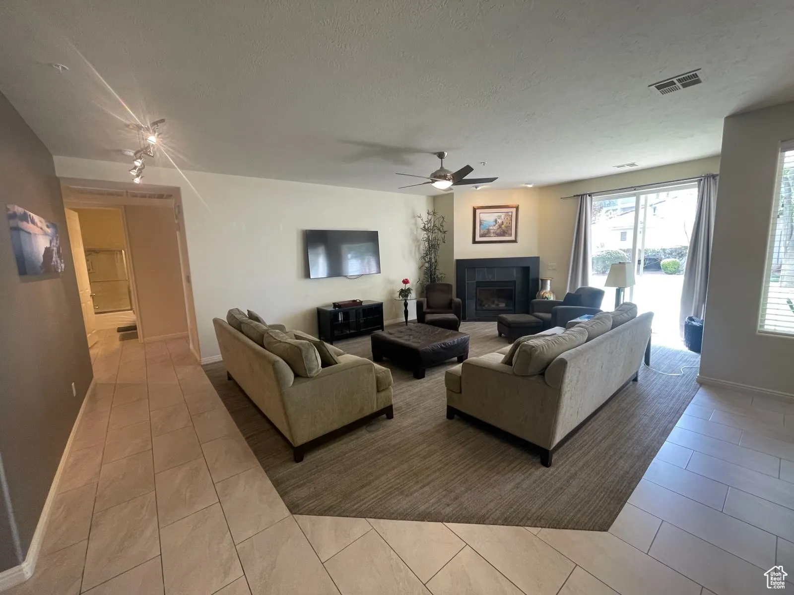 Tiled living room featuring a ceiling fan, a fireplace, and a textured ceiling