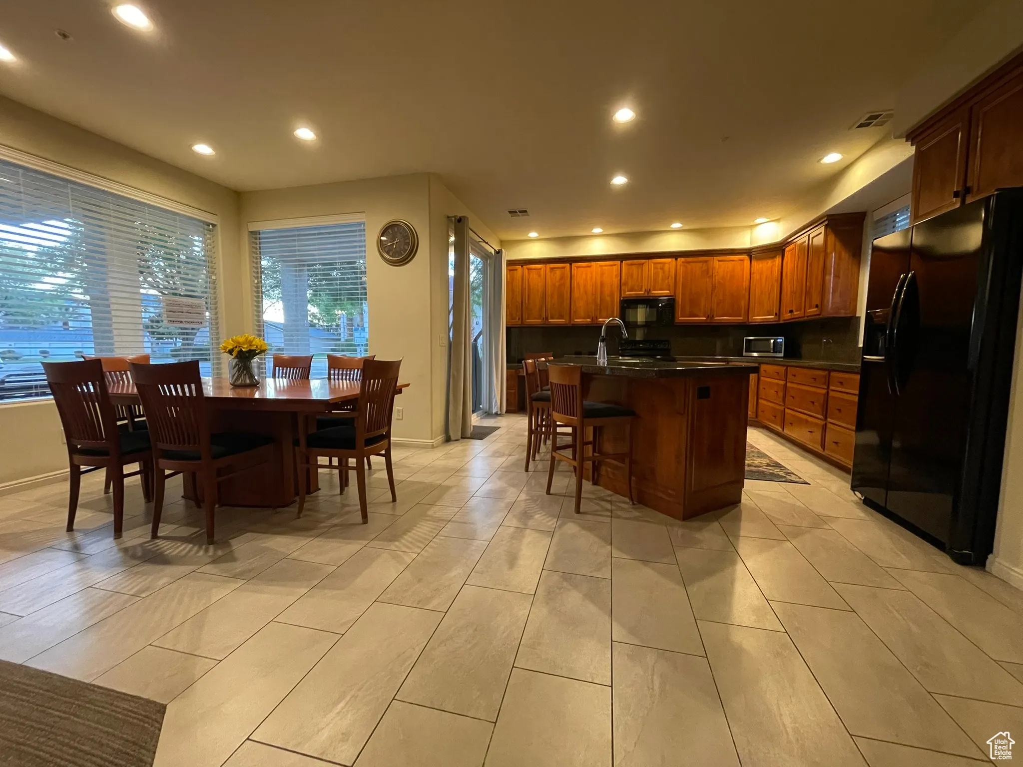 Kitchen with black appliances, recessed lighting, a breakfast bar, a kitchen island with sink, and brown cabinets
