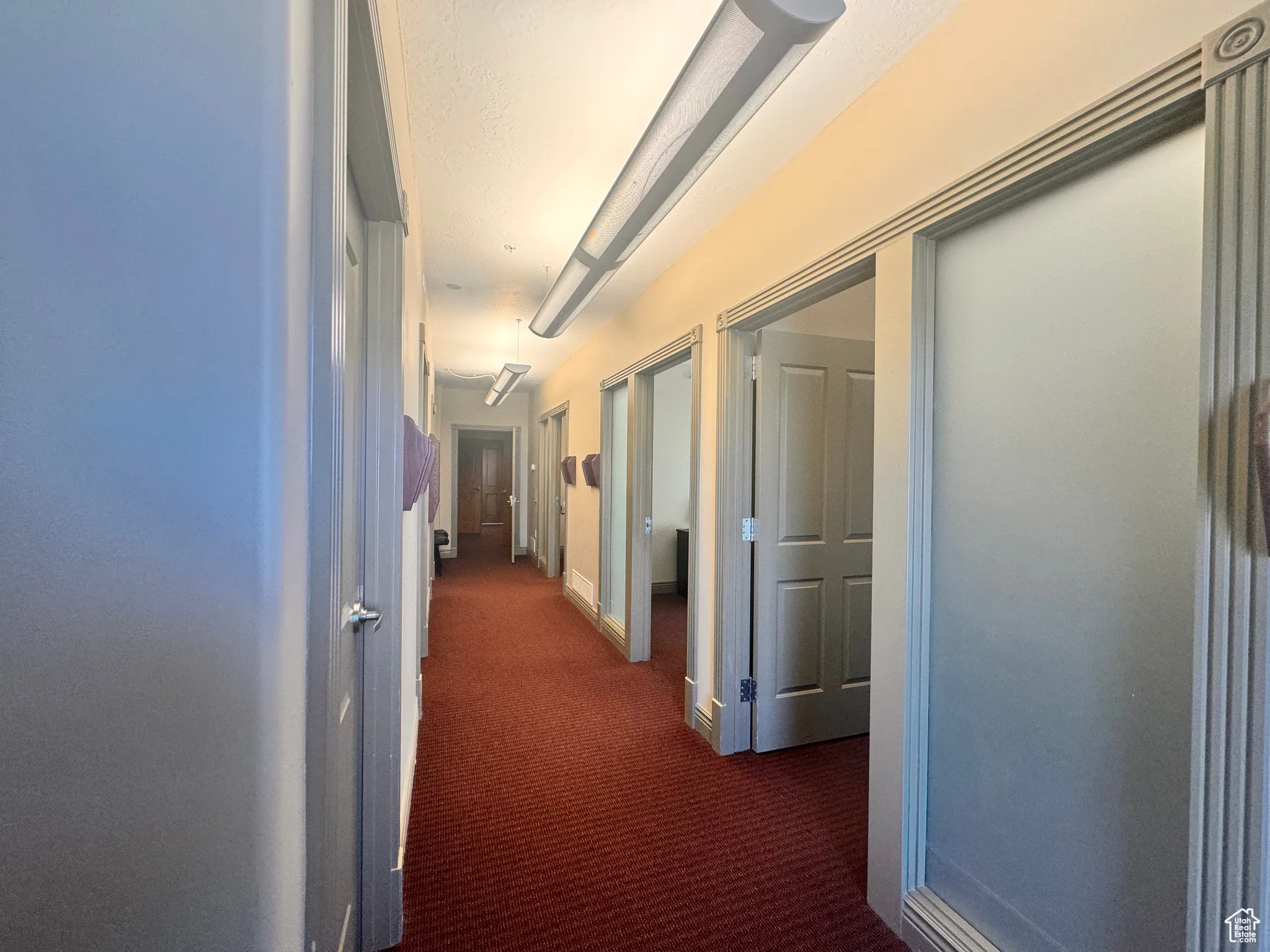 Hallway featuring dark colored carpet and baseboards