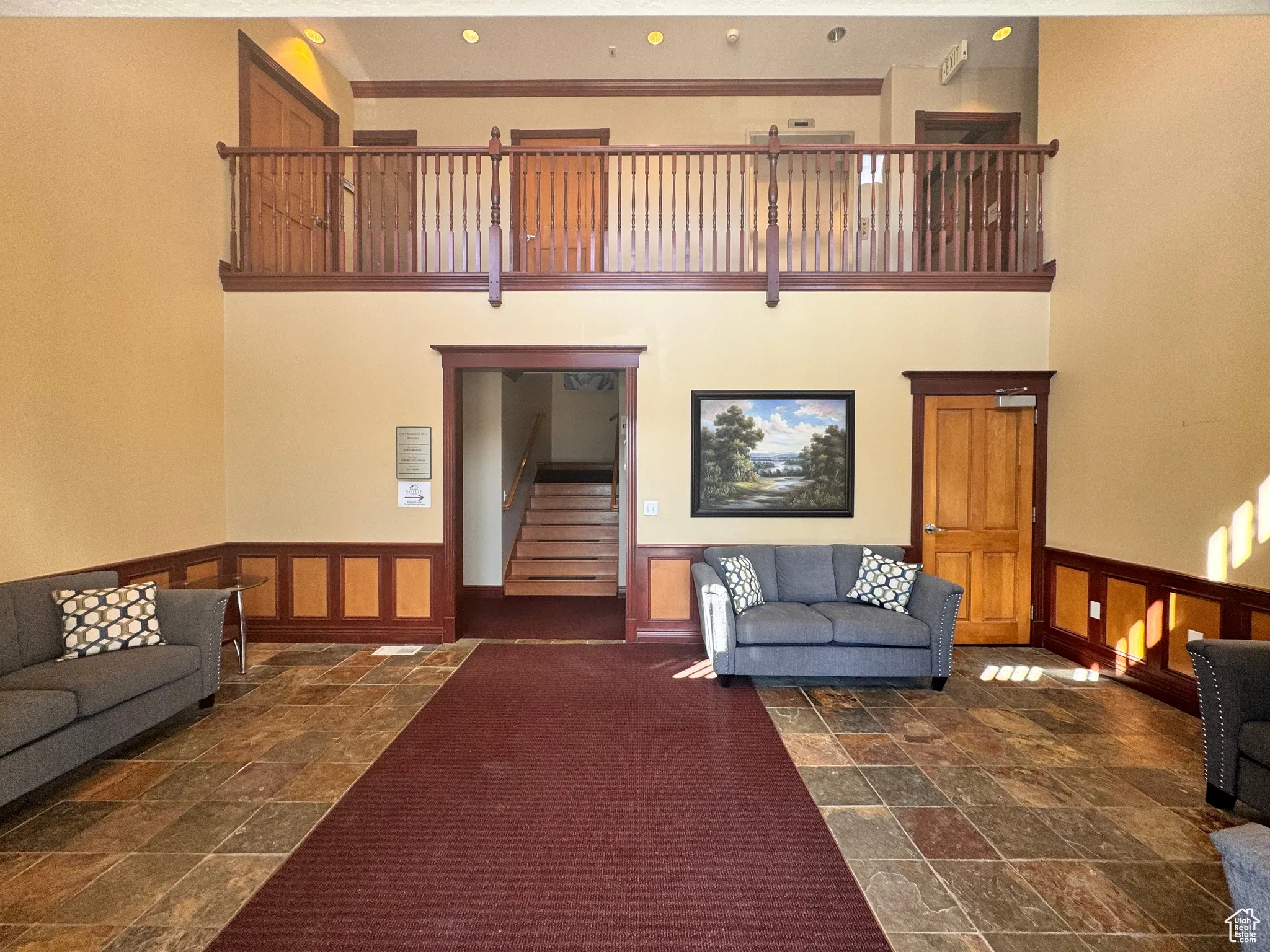 Living room with a wainscoted wall, a high ceiling, a decorative wall, stairs, and dark stone finish flooring