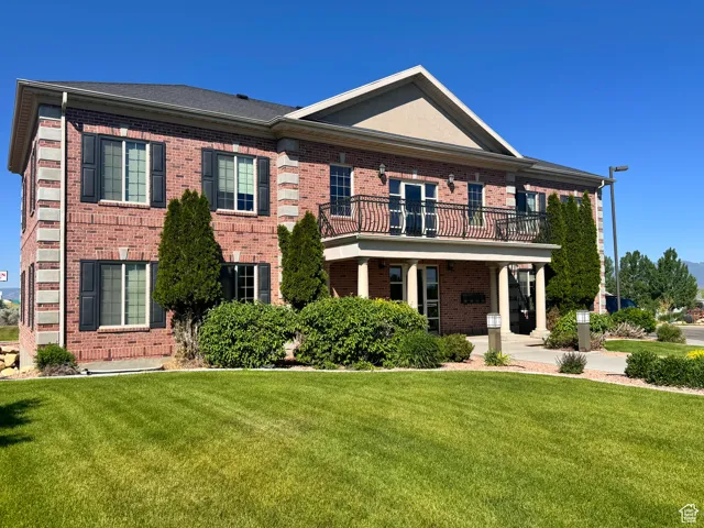 Georgian-style home featuring brick siding, a balcony, and a front yard
