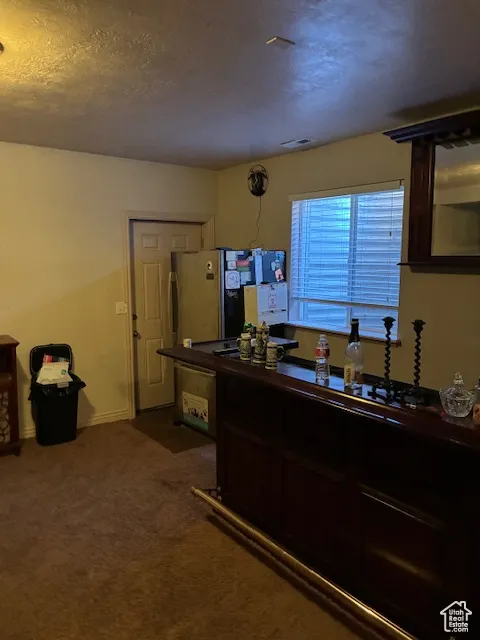 Kitchen with dark carpet, freestanding refrigerator, a textured ceiling, and dark countertops