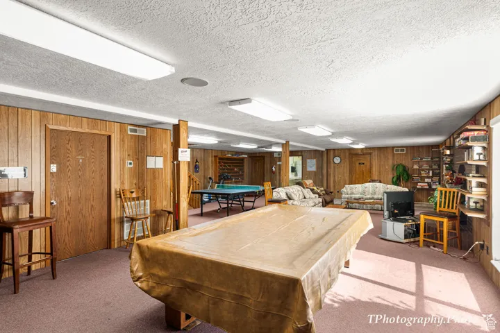Rec room with billiards table, carpet floors, wood walls, and a textured ceiling
