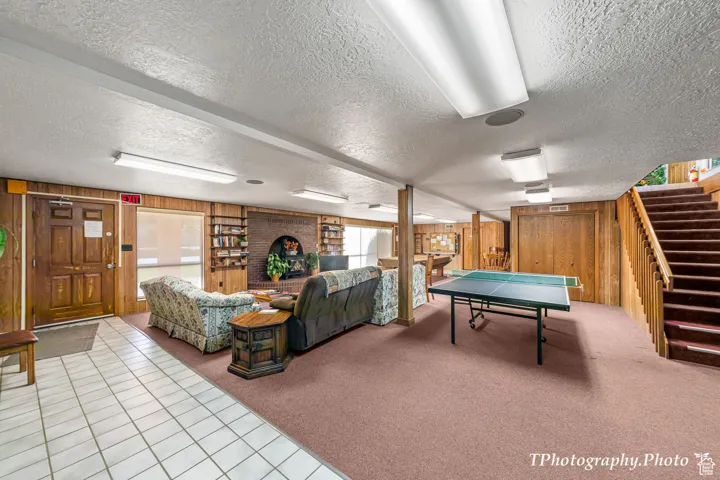 Game room featuring wooden walls, carpet, a textured ceiling, and tile patterned floors