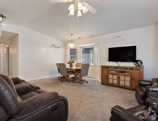 Carpeted living room with vaulted ceiling, a ceiling fan, and a chandelier