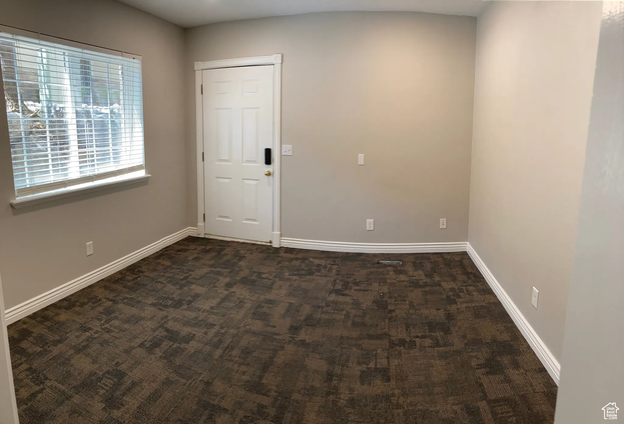 Unfurnished room featuring dark colored carpet and baseboards