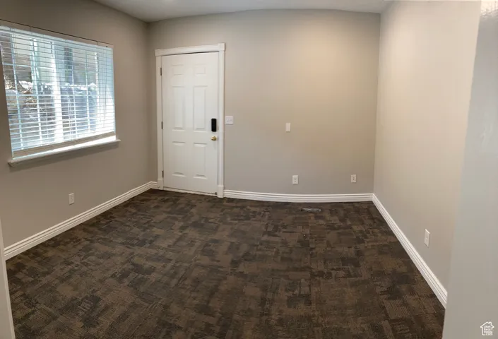 Unfurnished room featuring dark colored carpet and baseboards