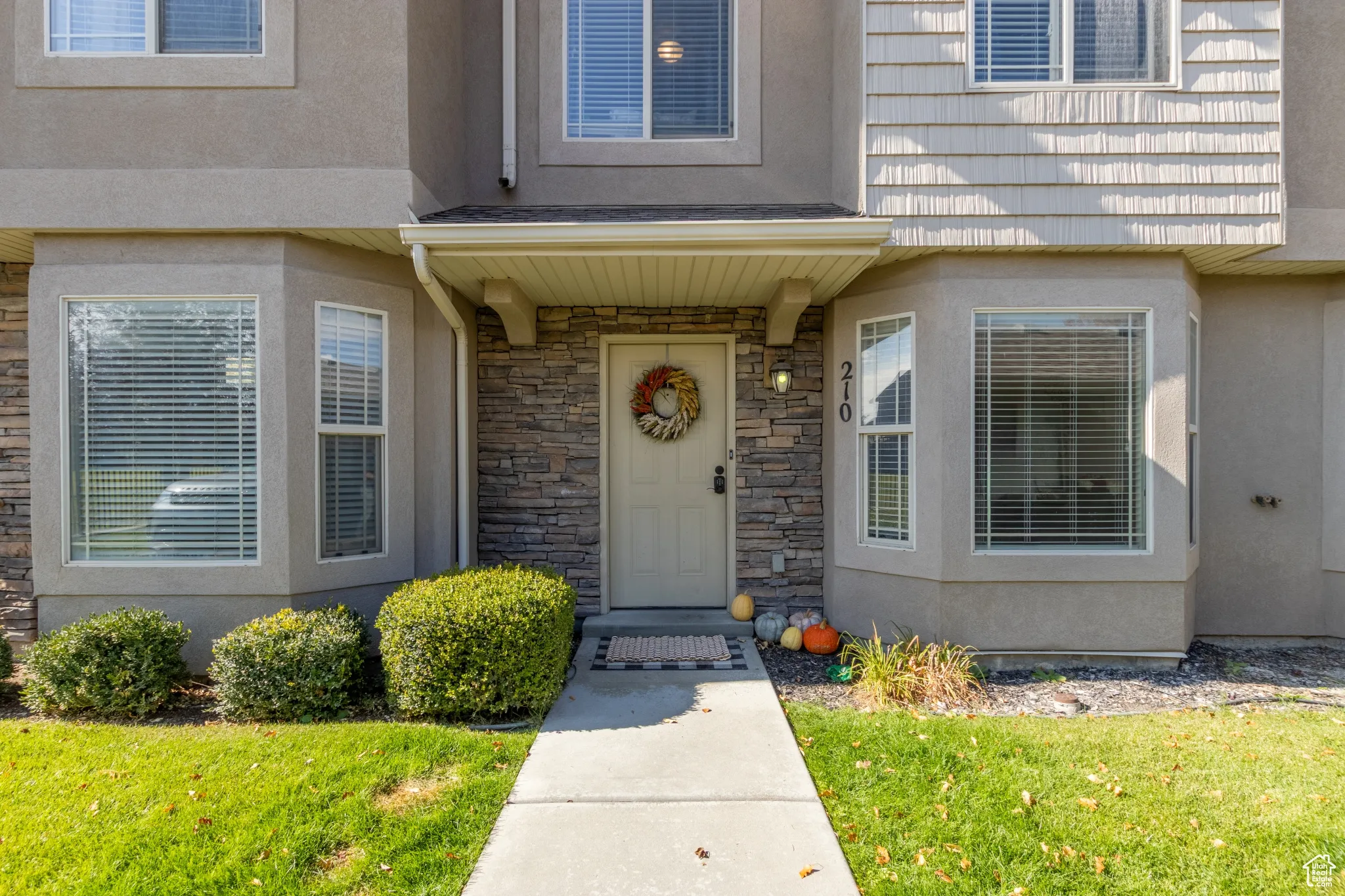 View of exterior entry with stucco siding, a lawn, and stone siding