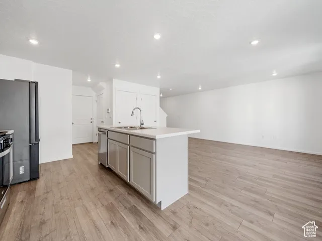 Kitchen featuring light countertops, light wood-style floors, recessed lighting, stainless steel appliances, and a kitchen island with sink